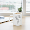 White mug with floral design on a desk next to a laptop