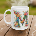 White mug with floral letter 'M' design on a wooden surface