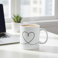 White mug with a heart design on a desk next to a laptop