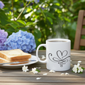 Steaming mug with a heart design on a wooden table outdoors with flowers and toast.