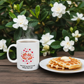 White mug with a heart design and waffles on a plate in front of white flowers