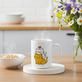 White mug with cat illustrations on a wooden table with a bowl of cereal and flowers in the background.